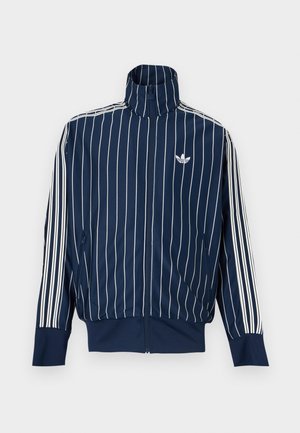 Marineblaue Jacke mit Reißverschluss, weißen vertikalen Nadelstreifen, drei weißen Streifen an den Ärmeln, hohem Kragen und Adidas-Trefoil-Logo auf der Brust.