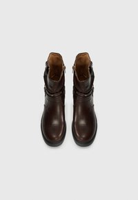 Pair of dark brown leather ankle boots with side zippers, decorative straps, and black rubber soles on a plain white background.