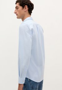 Lichtblauwe langarmshirt van katoen; voorzien van een kraag, knopenmanchetten en een rechte snit met een rugpand.