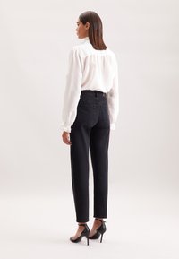 Czarna para spodni z wysokim stanem i prostymi nogawkami, z dwiema tylnymi kieszeniami, zestawiona z białą bluzką o fakturze i czarnymi sandałami na wysokim obcasie.