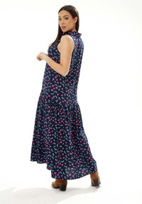 Navy blue sleeveless dress with pink and green floral pattern, round collar, flared hem, and soft fabric texture. Brown ankle boots visible.