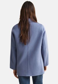 Cappotto in misto lana azzurro chiaro con taglio dritto, maniche larghe e pince posteriori. Presenta un colletto a revers e un design pulito e minimalista.