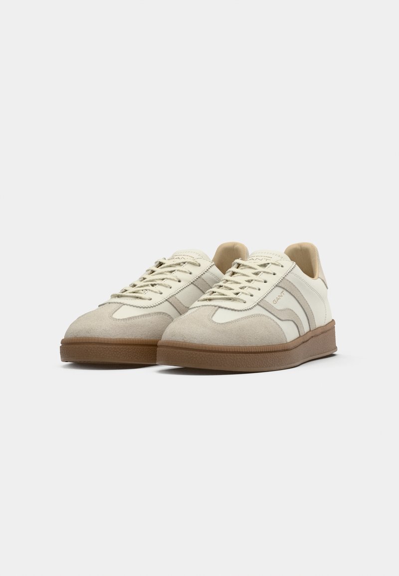 Beige Wildleder- und Ledersneaker mit einer strukturierten braunen Gummisohle, ausgestattet mit hellen Schnürsenkeln und dezentem Branding auf der Zunge.