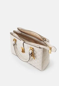 Beige quiltet håndtaske med guldfarvet hardware, dobbelt håndtag og to lynlåslommer. Glat finish med mønstret foring indeni.