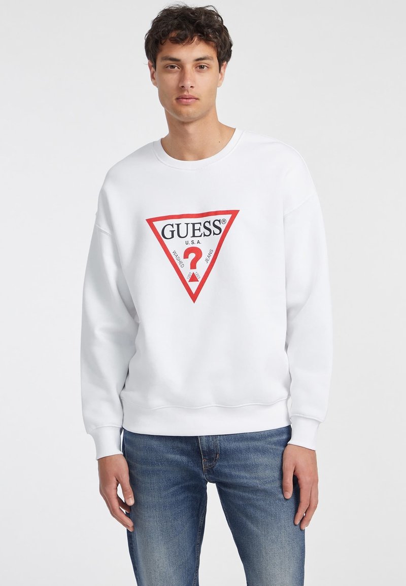Sudadera blanca con un logo triangular rojo que dice "GUESS U.S.A." y un signo de interrogación. Tejido suave con puños y cinturilla acanalados.
