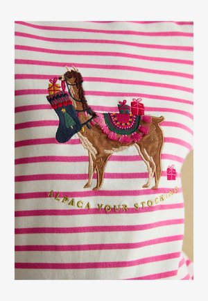 White fabric with pink stripes featuring an embroidered brown llama holding a stocking and gifts, with decorative accents and text below.