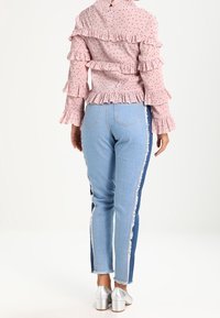 Růžová blůzka s volánky a vzorovanou texturou, kombinována s světle modrými džíny s třepenými okraji a kontrastními denimovými bočními panely. Stříbrné podpatky.