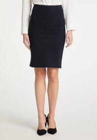 Marineblauwe kokerrok van rekbare stof, met een aansluitende snit en een lengte tot de knie. Gecombineerd met zwarte hoge hakken.