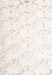 Bílá háčkovaná látka s opakujícím se vzorem mušlí a texturovaným povrchem, vytvářející otevřený, vzdušný vzhled.