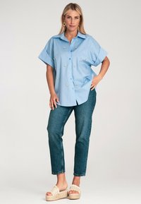 Jasnoniebieska koszula z krótkim rękawem z haftem kwiatowym, zestawiona z ciemnoniebieskimi dżinsami i jasnobeżowymi sandałami na platformie.