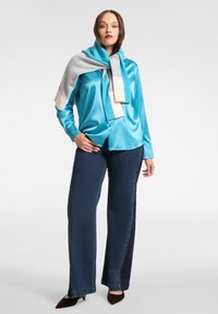 Turkusowa satynowa bluzka z długimi rękawami, zestawiona z ciemnoniebieskimi, szerokimi jeansami. Na ramionach luźno zarzucony jest szary i kremowy szal.