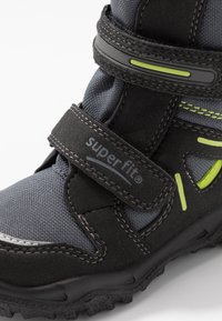 Stivale nero e grigio con tomaia in tessuto, cinturino in Velcro, dettagli riflettenti e accenti verde lime. Suola testurizzata per trazione.
