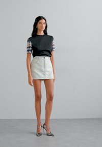 Haut noir avec des manches texturées, associé à une jupe courte à motifs dans des couleurs pastel. Des chaussures à talons hauts métalliques complètent la tenue.