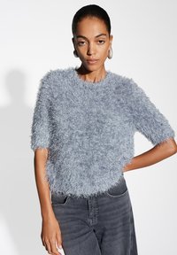 Fluffy light blue short-sleeve sweater with a round neck. Features textured, soft fabric. Worn with dark gray jeans.