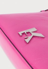 Spilgti rozā ādas rokassoma ar sudraba krāsas Karl Lagerfeld Paris logo emblēmu uz priekšējā vāka.