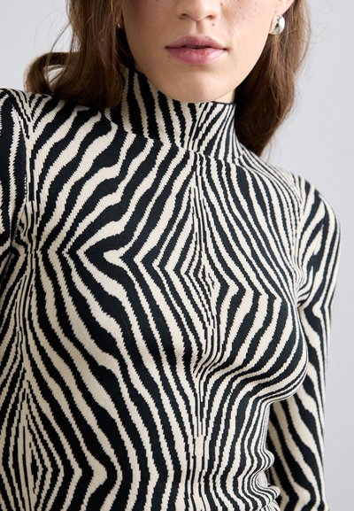 Μαύρο και άσπρο ριγέ πουλόβερ με ψηλό γιακά, που διαθέτει ριγωτή υφή και εφαρμοστή σχεδίαση. Διακρίνεται για το χαρακτηριστικό κυματιστό σχέδιο του.