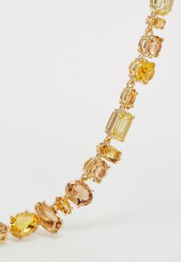 Gold bracelet with variously shaped yellow and amber gemstones set in prong settings on a white background.