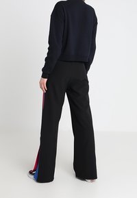 Pantalones de pierna ancha negros con paneles laterales en rojo y azul en contraste. Tejido suave y corte relajado, presentan una cintura alta y aberturas en el dobladillo.