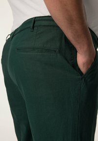 Pantaloni in cotone verdi con taglio dritto, dotati di tasca posteriore e una texture liscia. Vita con passanti per cintura, vestibilità rilassata.