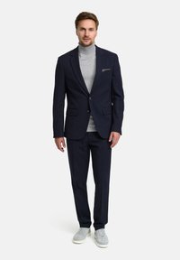 Granatowa marynarka o dopasowanym kroju, szary golf, spodnie w tym samym kolorze oraz jasnoszare sneakersy. Marynarka posiada kieszeń na piersi i gładką teksturę.