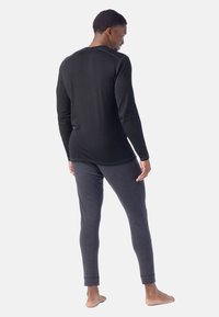 Svart långärmad topp som matchas med mörkgrå byxor. Båda är tillverkade av ett mjukt tyg, har en enkel design och en åtsittande passform, med uppvikta byxben.
