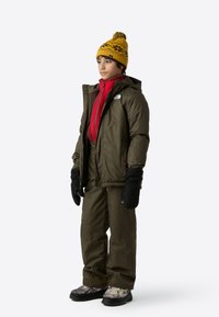 Insulated winter outfit featuring an olive green jacket and pants, red inner layer, black gloves, and a yellow patterned beanie. Textured boots.