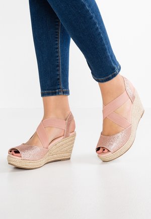 Fødder iført lyserøde glitrede kile-sandaler med krydsede elastiske stropper, kombineret med blå cropped skinny jeans.