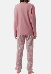 Pink long-sleeve top with relaxed fit and crew neckline paired with pink pants featuring a white ribbon pattern. Soft material, casual design.