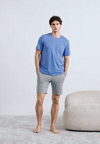 Camiseta azul de manga curta para homem, em material liso, combinada com calções cinzentos. A camisola apresenta um decote redondo e um detalhe subtil com logótipo.