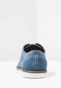 Scarpa in suede blu con punta rotonda, suola in gomma bianca, cuciture a contrasto e design a profilo basso, vista dalla parte posteriore.