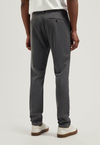 Sivé nohavice so slim fit strihom, s bočnými vreckami a kapsami na zips vzadu. V páre s bielymi teniskami, ktoré predvádzajú čistý dizajn.