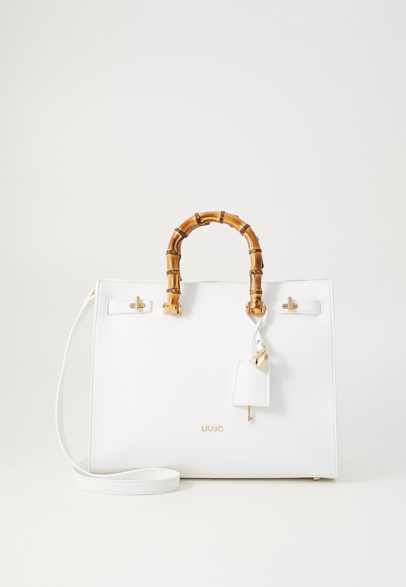 White handbag with bamboo handle, gold hardware accents, detachable tag, and thin shoulder strap. Smooth texture, structured design.