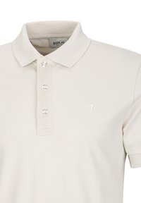 Lichtbeige polo shirt met een kraag, voorzien van drie knopen en een klein, wit "R" logo op de borst.