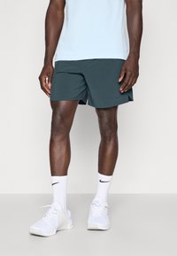 Pánske tmavozelené atletické šortky s voľným strihom, v kombinácii s bielymi teniskami a bielymi ponožkami s logom Nike. Hladká, ľahká tkanina.