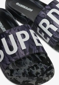 Zwarte en paarse slider sandalen met een textuurstof bovenkant voorzien van grote witte letters. Textuur zwarte zool voor grip.