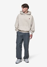Beige hoodie med frontlomme og lille logo, parret med grå løstsiddende bukser. Skoene er lys grå med et struktureret design.