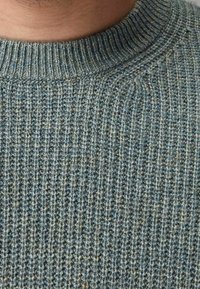 Strickpullover aus strukturiertem Material in sanften Blau-Grün-Tönen, mit einem gerippten Rundhalsausschnitt und einem weichen, warmen Stoff, der ein natürliches, abwechslungsreiches Muster aufweist.