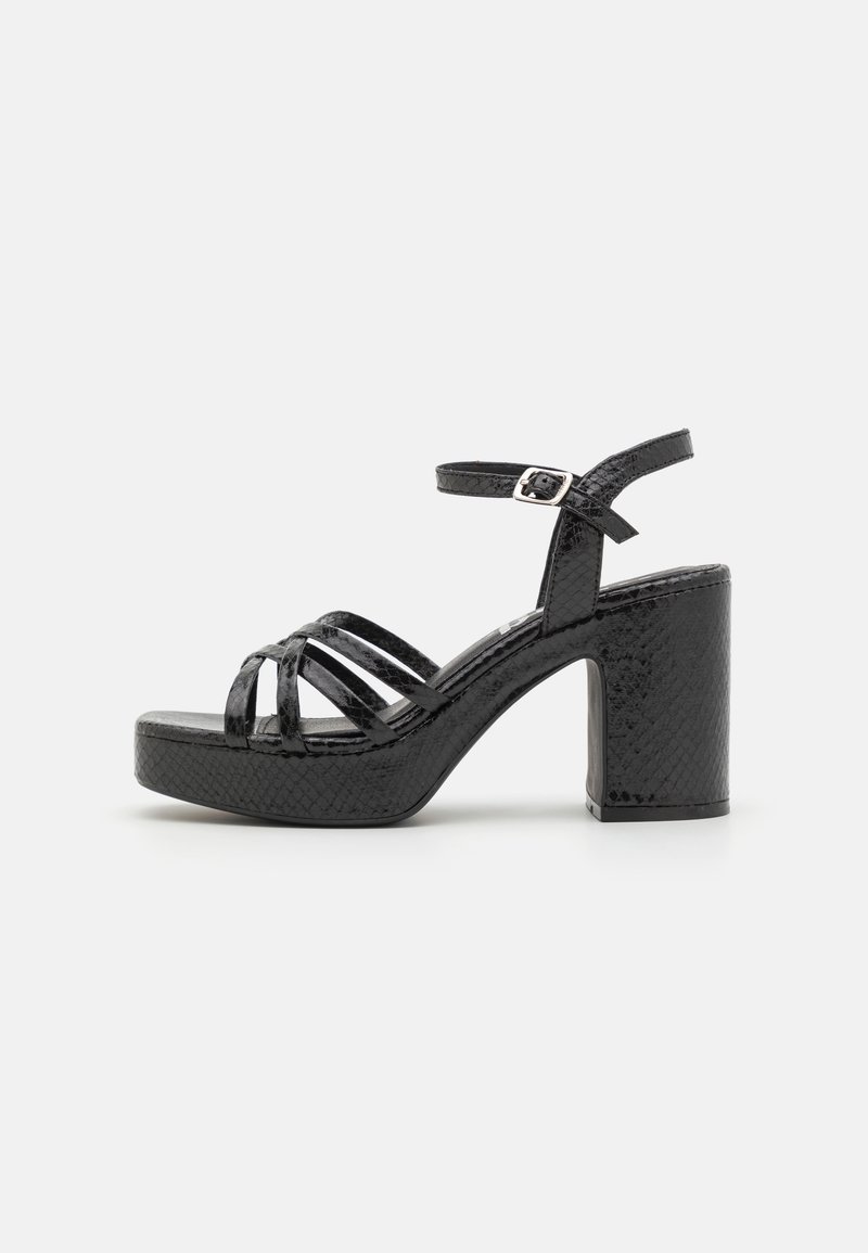 Sandalias negras de tacón con un grueso tacón cuadrado, con un acabado brillante y texturizado y múltiples correas entrelazadas. Correa ajustable en el tobillo con hebilla.
