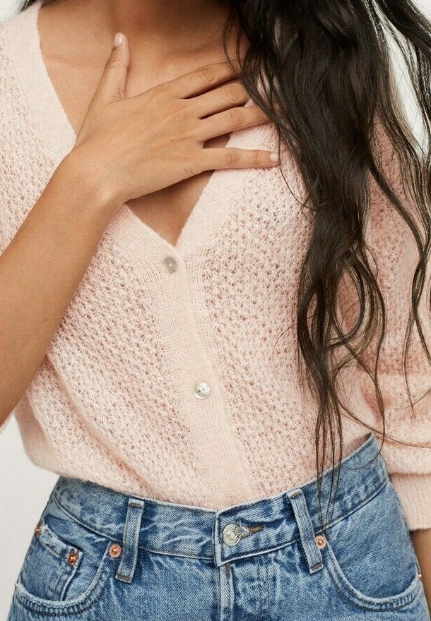 Helle rosa Strickjacke mit tiefem V-Ausschnitt und Knopfverschluss. Kombiniert mit hoch taillierten blauen Denim-Shorts.