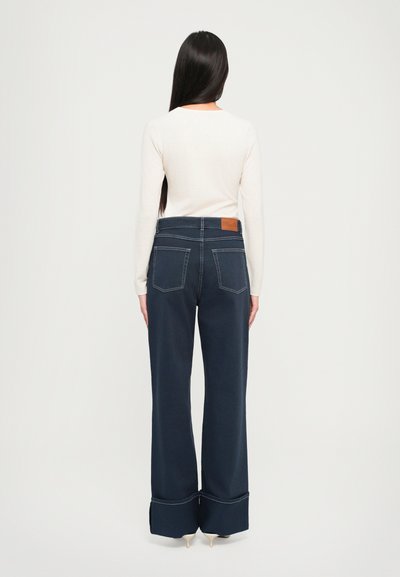 Námornícke široké džínsy s kontrastným prešívaním, dvoma zadnými vreckami a detailom prehnutého lemu. V kombinácii s bielym topom s dlhým rukávom.