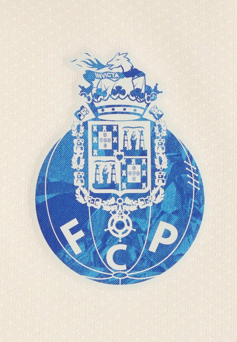 Blau-weißes Emblem des Fußballclubs FC Porto mit einem gekrönten Schild und einem Drachen darüber, vor einem beigen Stoffhintergrund.