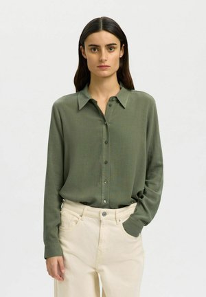 Langærmet olivegrøn bluse med knappelukning foran, krave og blød tekstur, kombineret med cremefarvede bukser med vide ben.