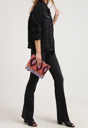 Veste en denim noir, jean noir évasé et sandales noires à talons. Tient une pochette à motifs colorés avec des accents roses, bleus et noirs.