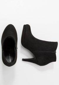 Bottines en daim noir avec un bout pointu, une fermeture éclaire sur le côté et un talon stiletto fin. Texture lisse avec un design minimaliste.