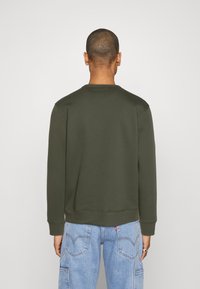 Sudadera verde oscura de manga larga, con cuello redondo y puños acanalados. Combinada con jeans de color azul claro que presentan un diseño clásico de cinco bolsillos.