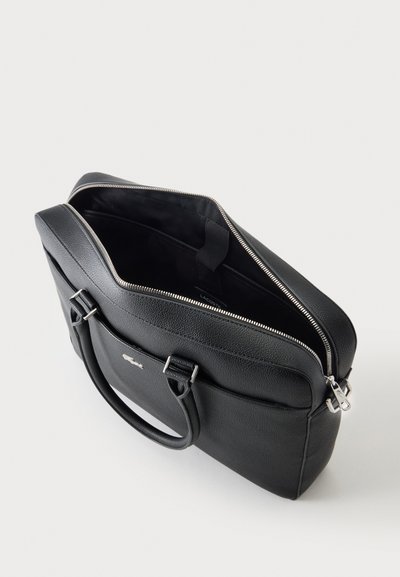 Porte-documents en cuir noir avec doubles poignées, fermeture éclair partiellement ouverte montrant un intérieur noir vide avec une petite poche intérieure.