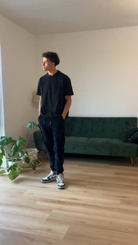 T-shirt noir et pantalon cargo noir, assortis avec des baskets multicolores. Canapé en velours vert et plante en pot dans une pièce lumineuse.