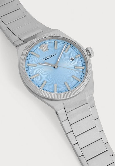 Montre-bracelet en métal argenté Versace avec un cadran bleu clair, des index argentés, une fenêtre date à 3 heures et un logo Versace Médusa à 12 heures.
