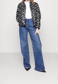 Pufferjakke i sort med hvidt skriftmønster, parret med højtaljede, lyseblå vide jeans og sorte spidse hæle.