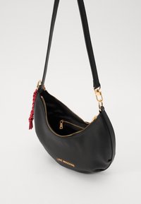 Black leather crossbody bag with a curved shape, gold zipper, and red braided accent. Logo "LOVE MOSCHINO" embossed on the front.